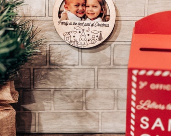 Könnte beinhalten: Ein Weihnachtsbaumschmuck aus Holz mit einem Foto von zwei Kindern und dem Text "Family is the best part of Christmas". Der Schmuck ist mit einem kleinen Haus, einem Weihnachtsbaum, einem Schneemann und Sternen verziert.