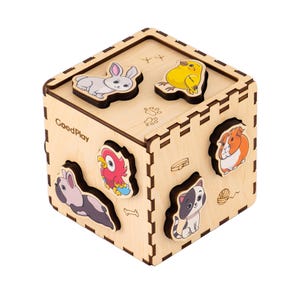 May include: Wooden cube puzzle featuring animal shapes: a rabbit, chick, parrot, guinea pig, cat, and dog. The cube has cut-out shapes for each animal. The brand name "GoodPlay" is printed on the side.