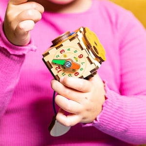 May include: A wooden toy with a colourful dial featuring numbers 0-9 and a green and orange pointer. The toy is held by a child's hand.