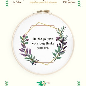 May include: Cross stitch pattern featuring a floral wreath with a gold geometric frame and the text "Be the person your dog thinks you are." The pattern is for Aida 14 count fabric and measures 10.2 inches by 9.1 inches. It uses 9 colors from the DMC palette.