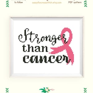 May include: Cross stitch pattern featuring a pink ribbon and the text "Stronger than cancer". The pattern is designed for Aida 14 fabric and measures 5.4 by 3.7 inches, or 13.6 by 9.3 centimeters. It requires two colors of thread and uses DMC floss.