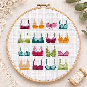 Könnte beinhalten: Ein Kreuzstich-Stickrahmen mit einer Sammlung farbenfroher, pixeliger BH-Designs. Die BHs sind in verschiedenen Stilen und Farben gehalten, darunter Rosa, Grün, Orange und Blau. Die Stickerei ist vor einem weißen Stoffhintergrund angeordnet.