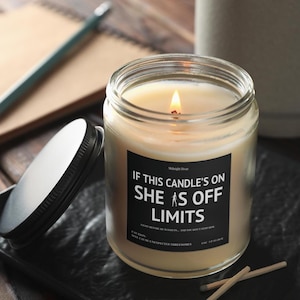 May include: A lit candle in a clear glass jar with a black label that reads "IF THIS CANDLE'S ON SHE IS OFF LIMITS." The candle is on a dark surface with a lid and matches nearby. The candle is 4 oz.