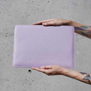 May include: A rectangular, solid light purple laptop sleeve with rounded corners and visible stitching along the edges. The sleeve features a smooth, matte finish and a clean, minimalist design, providing a simple protective cover for a portable computer.