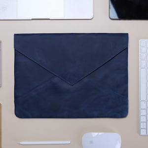 Op de afbeelding: Een donkerblauwe lederen laptophoes met een envelopvormige klepsluiting met een puntig midden. De hoes heeft een gladde, matte afwerking en is rechthoekig van vorm, ontworpen om een draagbare computer veilig in het gestructureerde frame te houden.