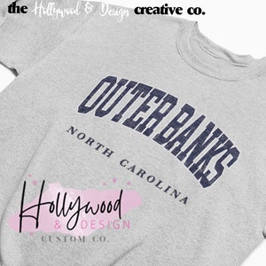 May include: Gray sweatshirt with a navy blue arch design that reads "Outer Banks North Carolina".