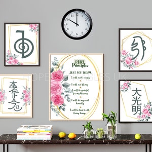 May include: A collection of framed Reiki art prints with floral accents and Japanese characters. The central print displays the Reiki Principles text. A black clock hangs above the prints, and the arrangement is set against a gray wall.