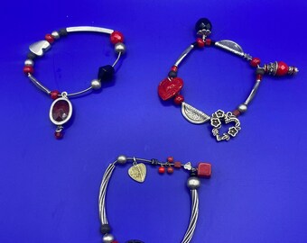 Ensemble de trois bracelets en métal. Bracelets avec pendentifs. Bracelets en métal avec différents pendentifs rouges.