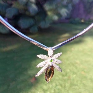 Può includere: Una collana d'argento con un ciondolo che presenta una pietra preziosa marrone a forma di lacrima circondata da un design floreale con pietre trasparenti.