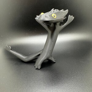 May include: Black 3D printed figurine of a dragon with yellow eyes. The dragon is standing on its hind legs with its front legs raised in the air.