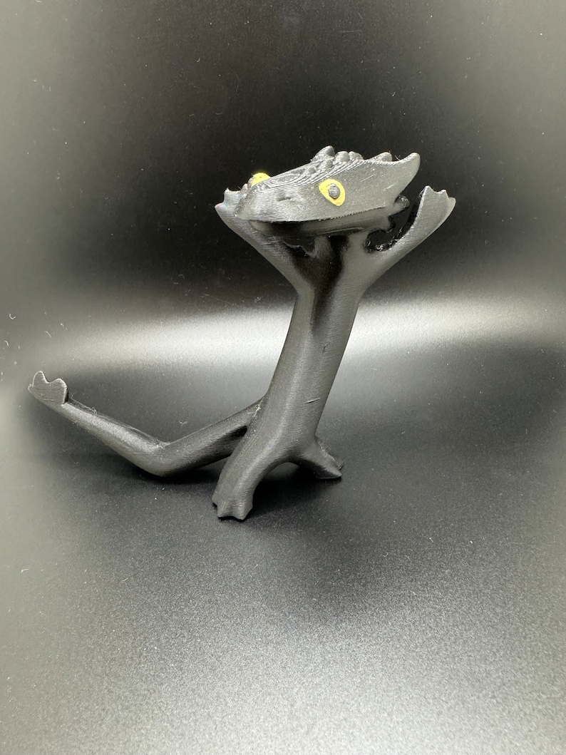 May include: Black 3D printed figurine of a dragon with yellow eyes. The dragon is standing on its hind legs with its front legs raised in the air.