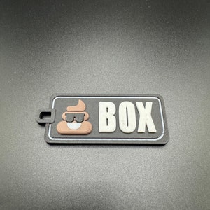 May include: A black and white patch with a brown poop emoji wearing sunglasses and the word "BOX" in white letters.