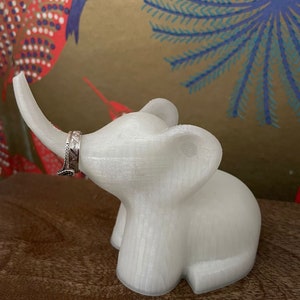 Op de afbeelding: Witte keramische olifanten ringhouder met een getextureerd oppervlak. De slurf van de olifant is opgerold en een zilveren ring is op de slurf geplaatst.