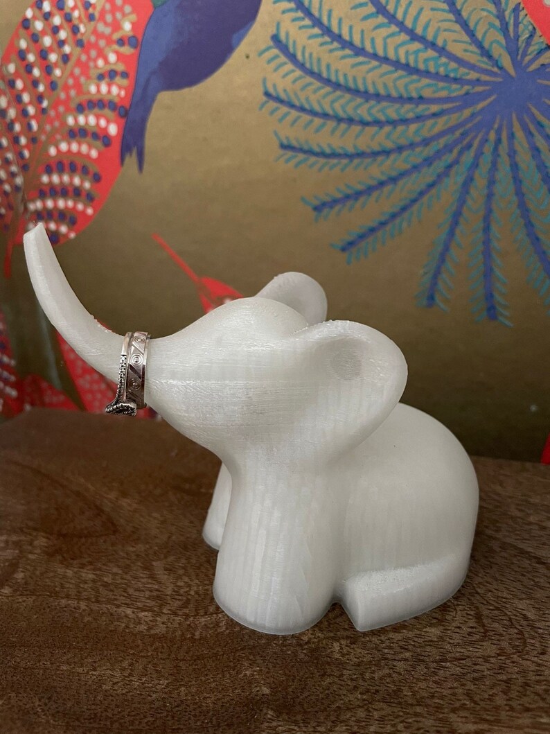 Op de afbeelding: Witte keramische olifanten ringhouder met een getextureerd oppervlak. De slurf van de olifant is opgerold en een zilveren ring is op de slurf geplaatst.