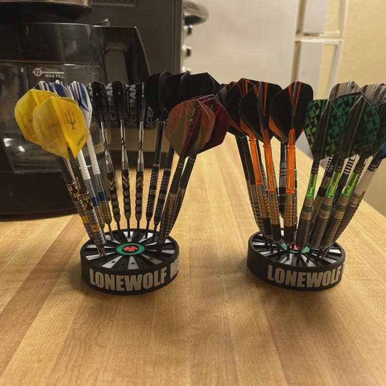 May include: Two dart holders with multiple darts. The holders are black with the word "LONEWOLF" in white. The darts have various colors, including yellow, black, orange, and green. The darts are arranged in a fan-like pattern.