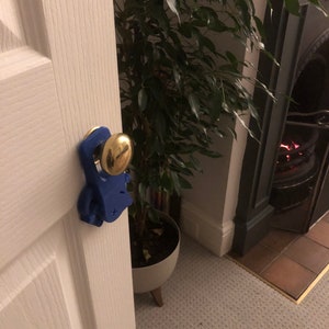 May include: A blue doorstop shaped like a person with a gold door knob. The doorstop is attached to a white door.