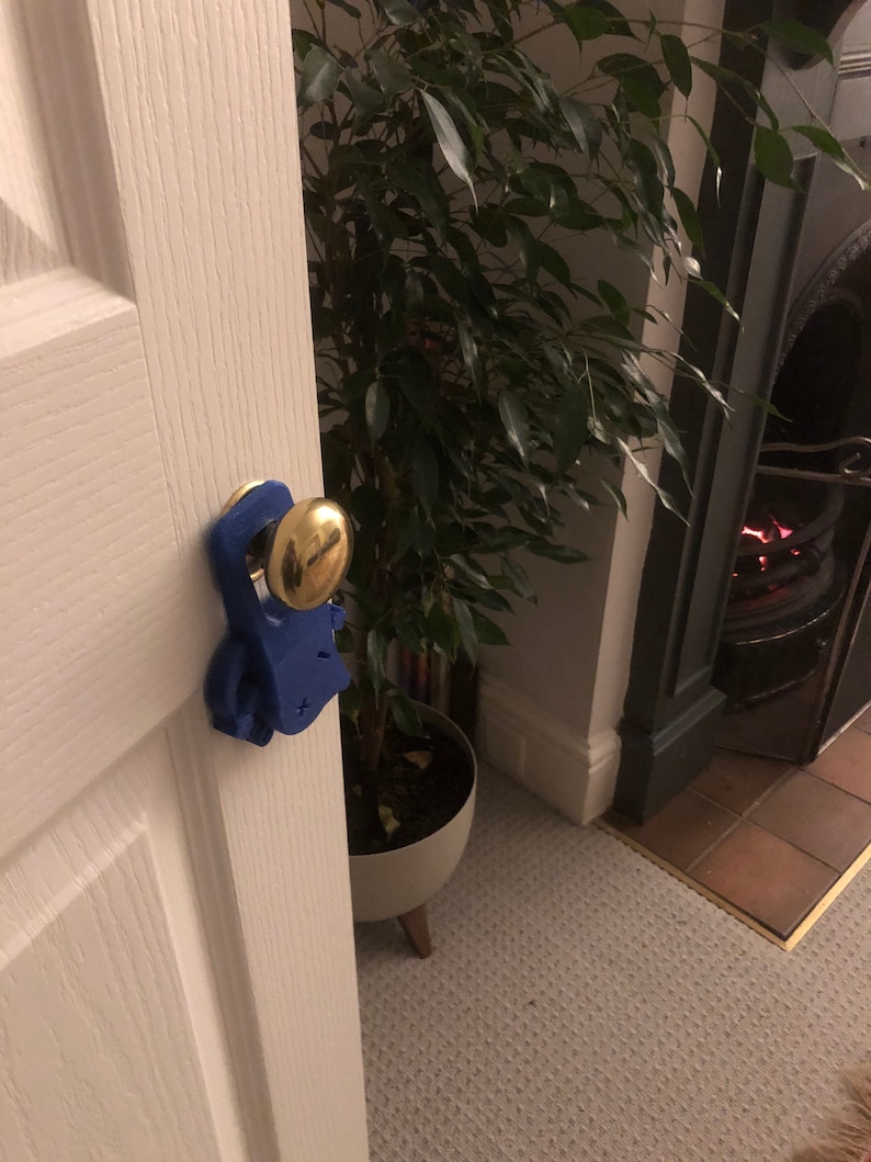 May include: A blue doorstop shaped like a person with a gold door knob. The doorstop is attached to a white door.