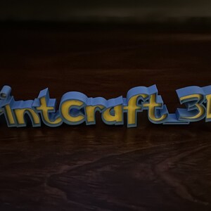 May include: A blue and yellow 3D printed sign that reads "PrintCraft 3D".
