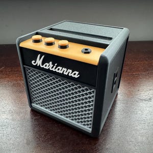 May include: A black and gray miniature guitar amplifier with a yellow trim and the word "Marianna" printed on the front.
