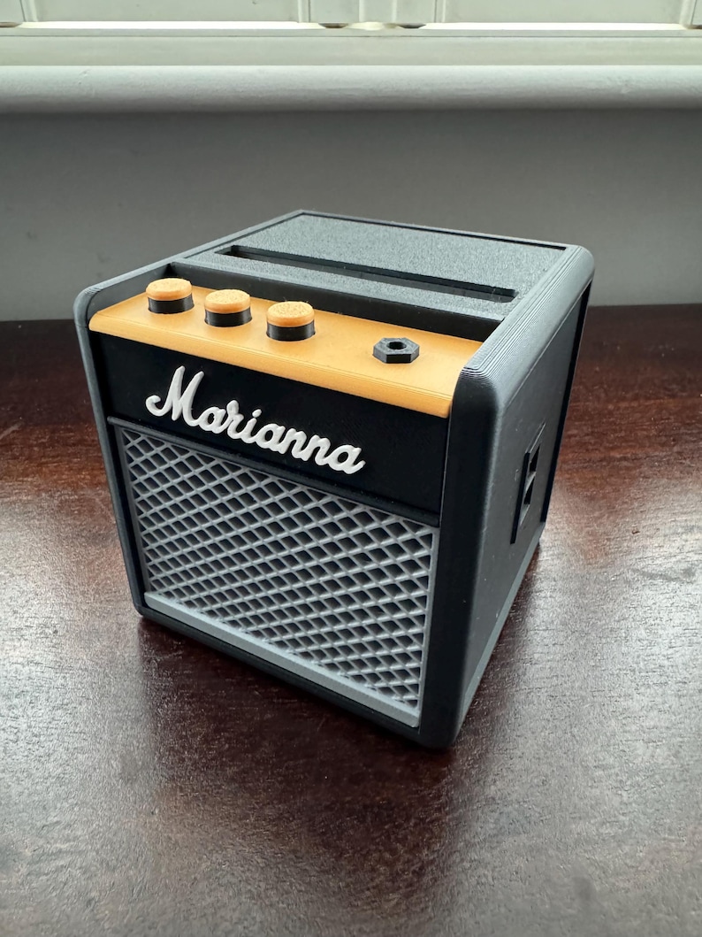 May include: A black and gray miniature guitar amplifier with a yellow trim and the word "Marianna" printed on the front.