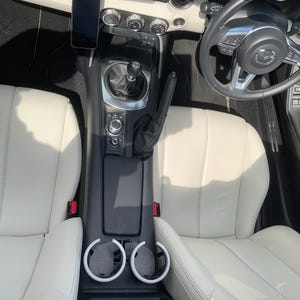 K&ouml;nnte beinhalten: Innenansicht eines Autos mit cremefarbenen Ledersitzen und einem schwarzen Armaturenbrett. Das Bild zeigt das Lenkrad, den Schalthebel und die Mittelkonsole mit Getr&auml;nkehaltern. Ein Smartphone ist am Armaturenbrett befestigt.