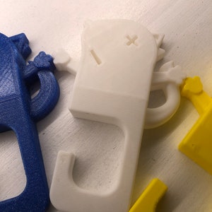 May include: Three 3D printed doorstop hooks in the shape of a cartoon cat. The hooks are blue, white, and yellow.