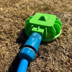 May include: A green sprinkler head with a blue hose connector attached to a blue hose. The sprinkler head is on a bed of dry grass.
