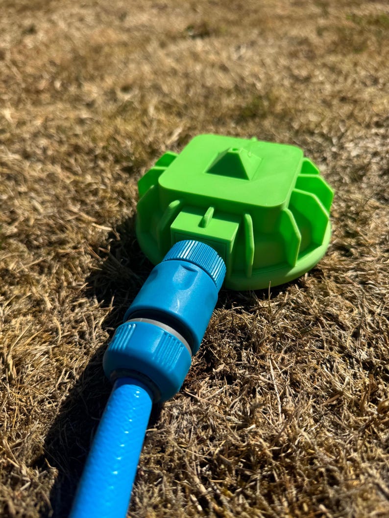 May include: A green sprinkler head with a blue hose connector attached to a blue hose. The sprinkler head is on a bed of dry grass.