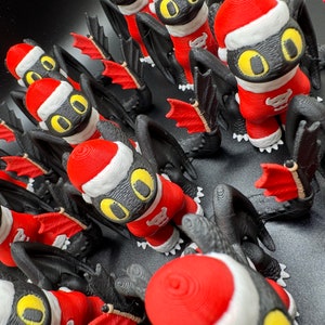May include: A group of black and red Christmas ornaments shaped like dragons wearing Santa hats. The ornaments have yellow eyes and are made of 3D printed plastic.