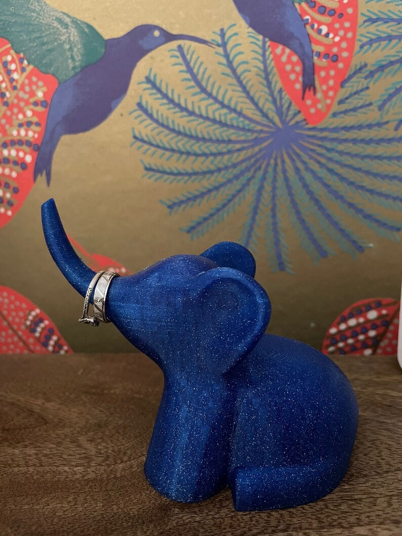 Op de afbeelding: Een blauwe glitter olifant ringhouder. De olifant heeft een opgetrokken slurf en een ring is op de slurf geplaatst.