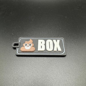May include: A black and white patch with a brown poop emoji and the word "BOX" in white letters.