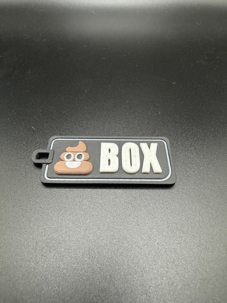 May include: A black and white patch with a brown poop emoji and the word "BOX" in white letters.