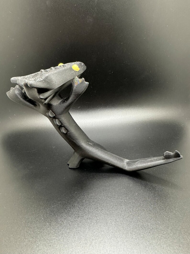 May include: A black 3D printed dragon figurine with yellow eyes. The dragon is posed in a standing position with its head tilted back and its tail curled around its body.