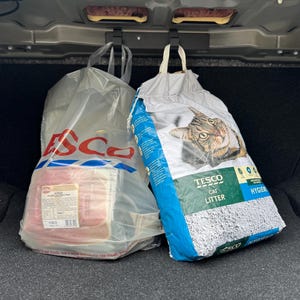 以下が含まれることがあります： 車のトランクにある2つの買い物袋。Tescoのロゴが入った透明なビニール袋には、包装された肉が入っています。もう一方の袋は、猫の画像と青と白のデザインのTesco猫用トイレ砂の袋です。