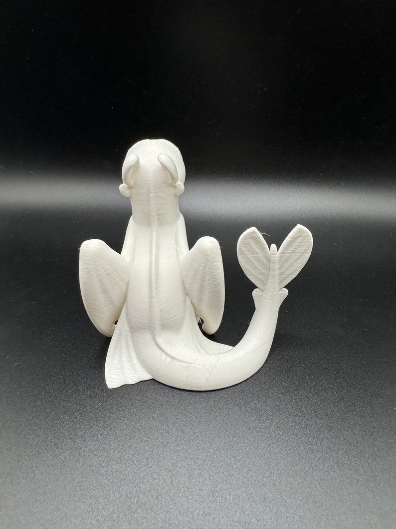 May include: White 3D printed figurine of a dragon with wings and a tail. The dragon is sitting on its hind legs with its head tilted back.