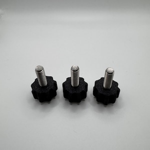 May include: Three black star-shaped knobs with silver threaded bolts. The knobs are made of a textured plastic material. The bolts are made of a shiny metal. The knobs are evenly spaced against a white background.