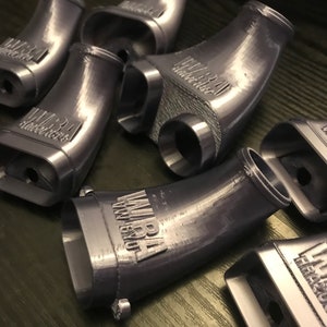 May include: A set of six gray 3D printed plastic parts with the text "MIRA" printed on each part. The parts are shaped like curved tubes.
