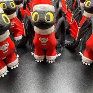 May include: A group of black and red Christmas-themed figurines of a dragon with white accents. The dragon figurines are wearing Santa hats and have a red and white Santa suit.