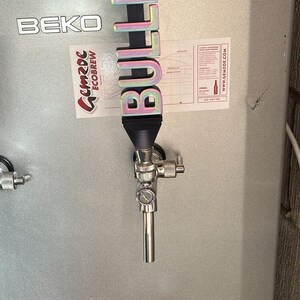 May include: A silver tap handle with a colourful 3D printed sign that reads "BULLISH" attached to it. The tap handle is attached to a silver tap on a silver refrigerator.