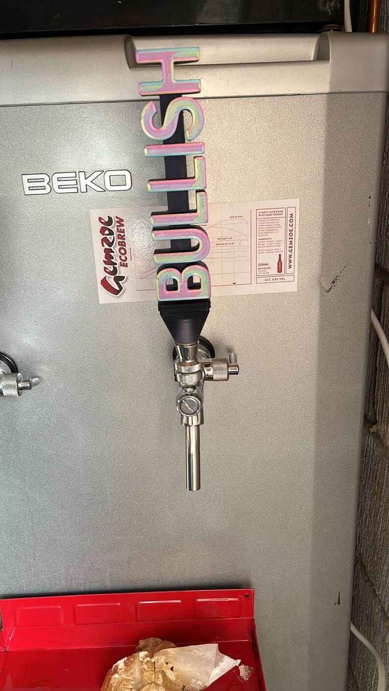May include: A silver tap handle with a colourful 3D printed sign that reads "BULLISH" attached to it. The tap handle is attached to a silver tap on a silver refrigerator.