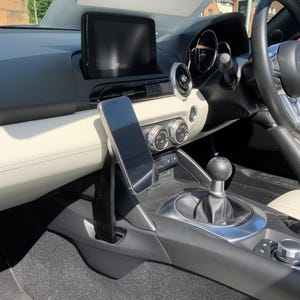 K&ouml;nnte beinhalten: Innenansicht eines Autos mit Smartphone-Halterung, zentralem Display und Bedienelementen. Das Armaturenbrett ist schwarz und cremefarben, mit Fokus auf Lenkrad und Schalthebel. Der Innenraum ist gut beleuchtet.