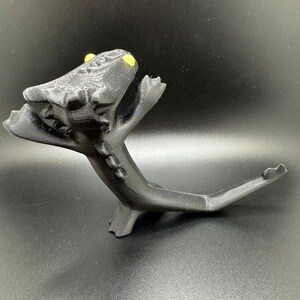 May include: Black 3D printed figurine of a dragon with yellow eyes, standing on its hind legs with its tail curled up behind it.