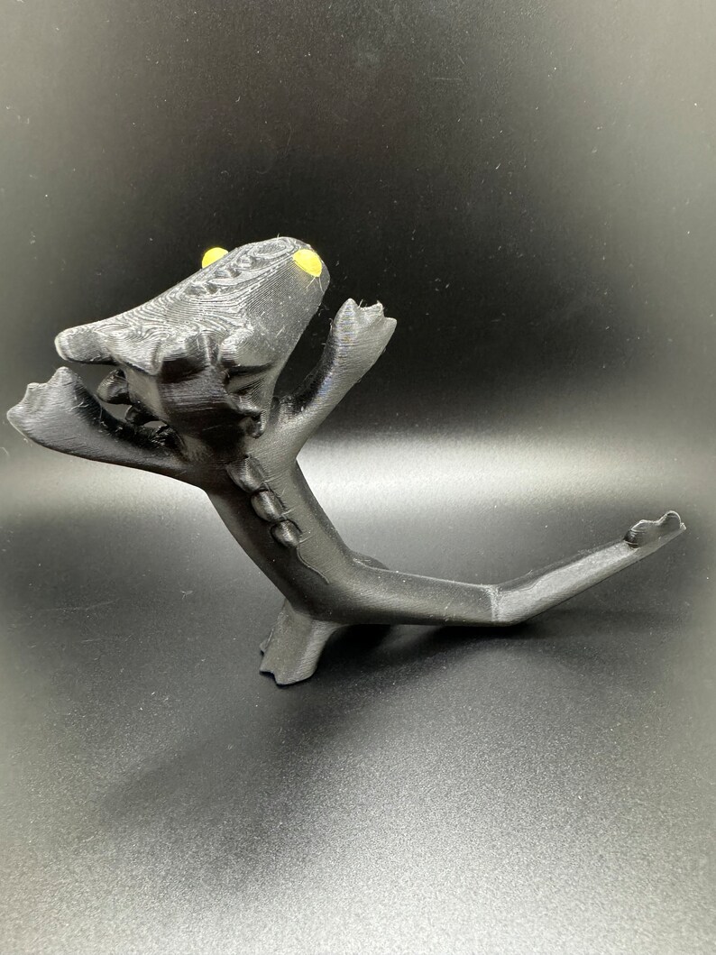 May include: Black 3D printed figurine of a dragon with yellow eyes, standing on its hind legs with its tail curled up behind it.