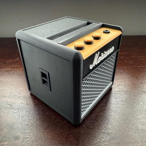 May include: A black and orange small guitar amplifier with the word "Marshall" printed on the front. The amplifier has three knobs on the top.