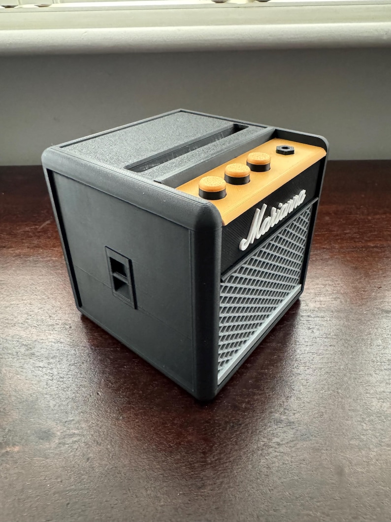 May include: A black and orange small guitar amplifier with the word "Marshall" printed on the front. The amplifier has three knobs on the top.