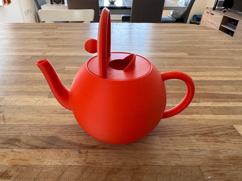 May include: A vibrant red teapot with a rounded body, a curved spout, and a handle. The lid features a unique design with a vertical handle and a small knob. This teapot is designed for brewing tea.
