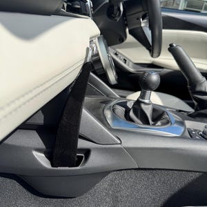 May include: Interior view of a car, showcasing the dashboard, steering wheel, and gear shift. The image highlights the black and white color scheme, with a focus on the seat belt and the car's interior design. The steering wheel is black, and the seats are white.