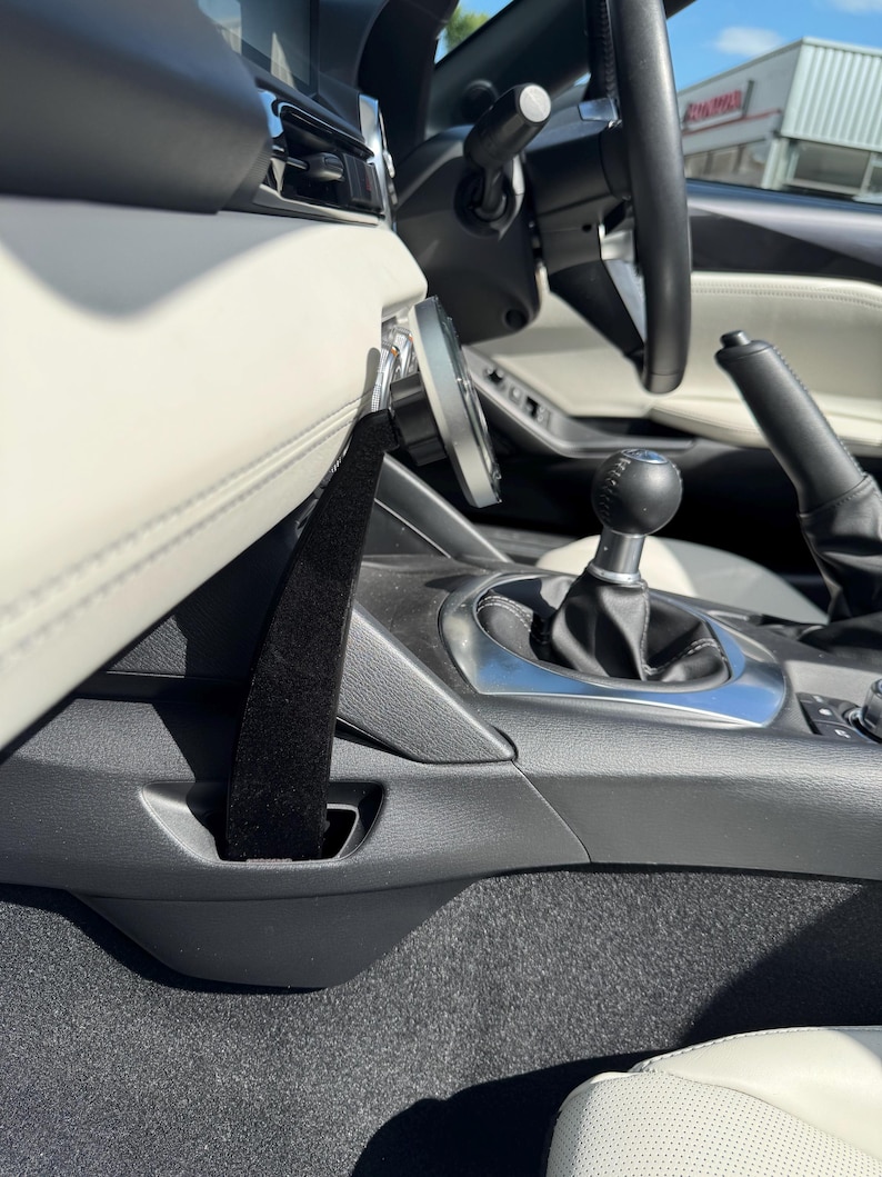 May include: Interior view of a car, showcasing the dashboard, steering wheel, and gear shift. The image highlights the black and white color scheme, with a focus on the seat belt and the car's interior design. The steering wheel is black, and the seats are white.