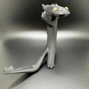 May include: Black plastic figurine of a dragon with yellow eyes. The dragon is standing on its hind legs with its tail curled around its front legs.