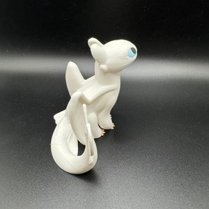 May include: White dragon figurine with blue eyes and a curled tail. The dragon is standing on a black surface.